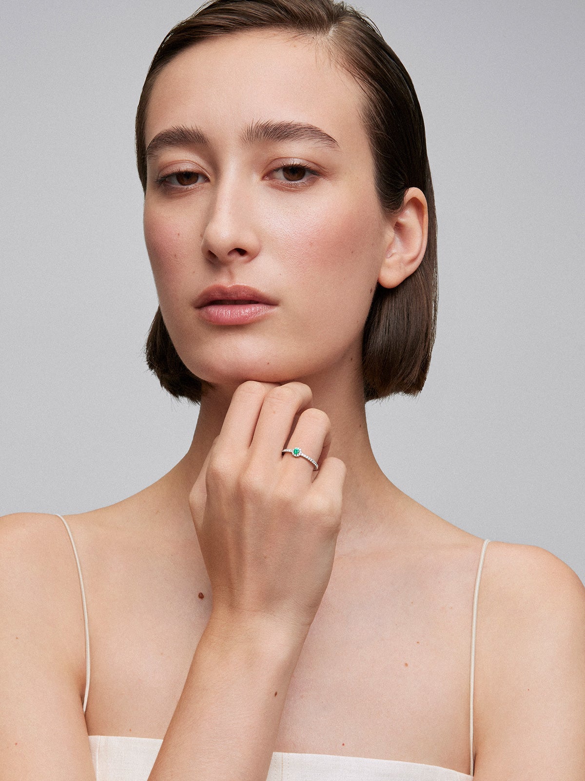 Anillo de oro blanco de 18K con esmeralda en talla brillante de 0,1 cts y brazo y orla de 28 diamantes en talla brillante con un total de 0,18 cts